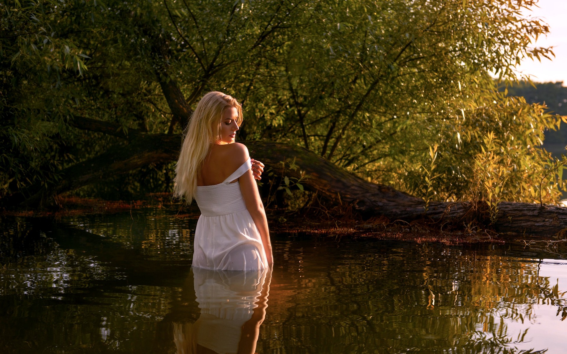 Стройная блондинка на озере красиво позирует обнаженной